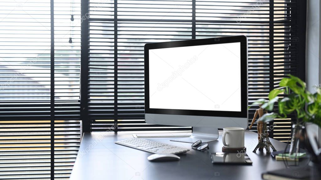 Computer with blank screen, coffee cup, houseplant and stationery on black wooden table in modern home office