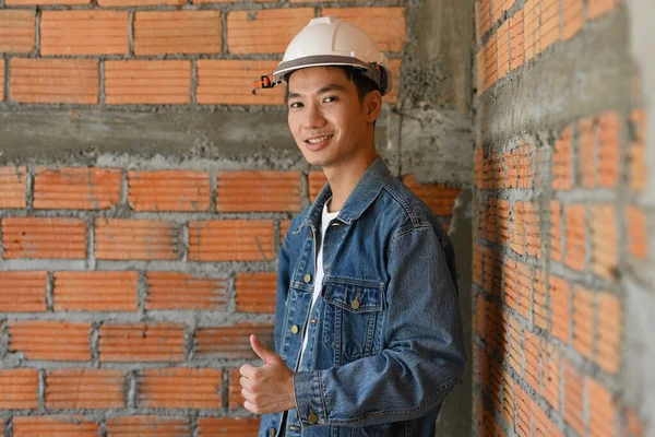 Kasklı Asyalı mimar inşaat alanında kameraya gülümsüyor. Endüstri, Mühendis, inşaat konsepti