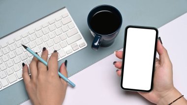 Yukarıda iş kadını cep telefonu tutuyor ve kablosuz klavyeyle yazı yazıyor..