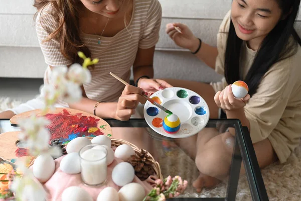 Petite fille mignonne et mère colorient les œufs se préparant pour la célébration de Pâques à la maison ensemble. — Photo