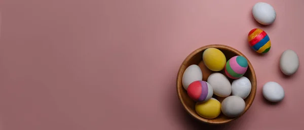 A wooden bowl full of Easter eggs on pink background with copy space for text or design. — Stock Photo, Image