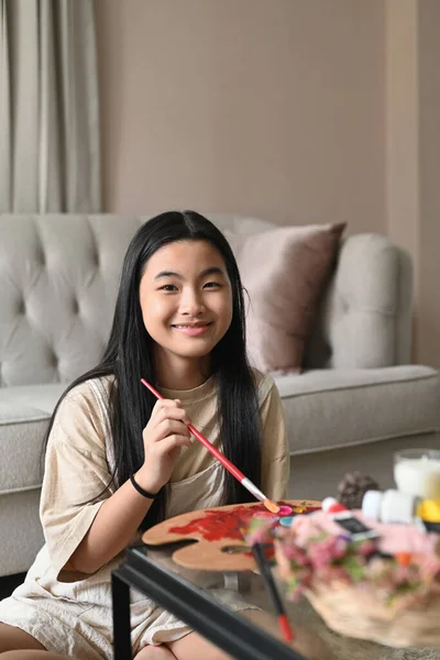 Söt asiatisk flicka sitter på golvet i vardagsrummet och målning bild med akvarell. — Stockfoto