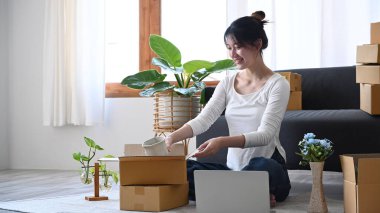 Genç bayan küçük işletme girişimcisi müşterilere teslimat için karton kutuda ürün paketliyor. Online satış, e-ticaret