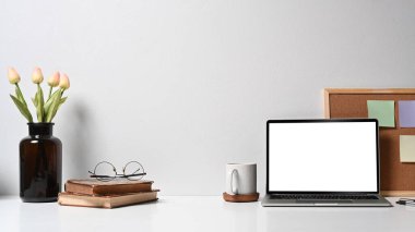 Laptop bilgisayarı, kahve fincanı, saksı ve beyaz masadaki kırtasiye malzemesi olan çağdaş işyeri