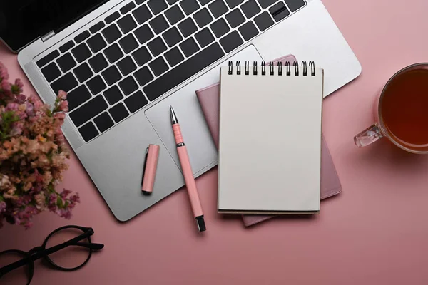 Lieu de travail féminin avec ordinateur portable, ordinateur portable, tasse à café et verres sur fond rose. — Photo