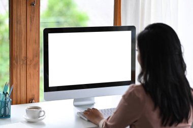 İş yerinde modern bilgisayarla çalışan yaratıcı bir kadının arka görünüşü.