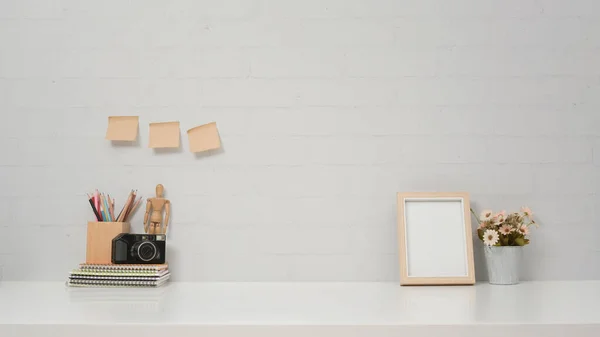 Contemporary workspace with camera, picture frame and flower pot on white table against brick wall. — Stock Photo, Image