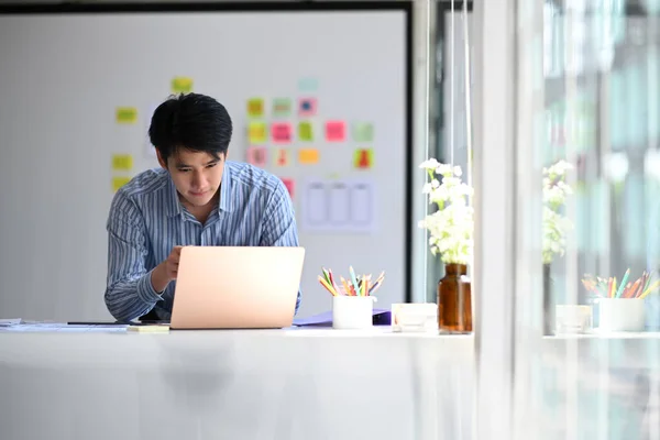 Young asian male web developer working on mobile application software design project at modern workplace.