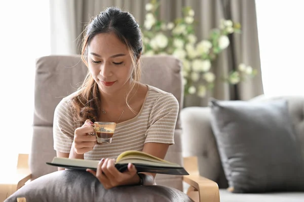 Relajada mujer tranquila beber café y leer libro en sillón cómodo. — Foto de Stock