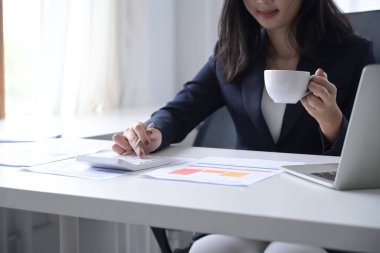 Kahve içen ve ofis masasında hesap makinesi kullanan kadın mali danışman..