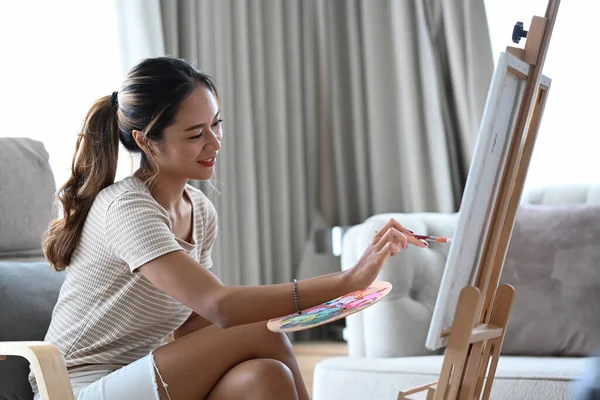 Attrayant asiatique femme en casual vêtements assis dans salon et profiter de la création de son artwork. — Photo