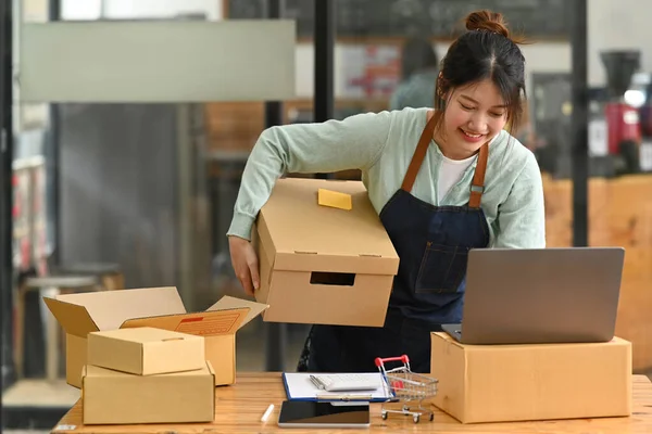 Startup small business owner checking or accepting orders on her laptop and preparing packages for delivery. Online selling, E-commerce