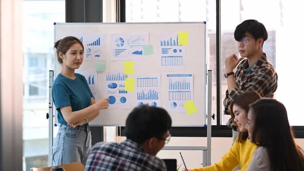 Mujer confiada de pie cerca del rotafolio con su colega y dando la presentación de una nueva estrategia de marketing. — Foto de Stock