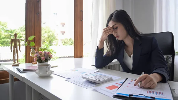 Young businesswoman looking worried, tired and overwhelmed while working at office desk. — Stock Photo, Image