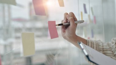 İşadamı parlak modern ofisteki yapışkan notlar hakkında yeni fikirler yazıyor..