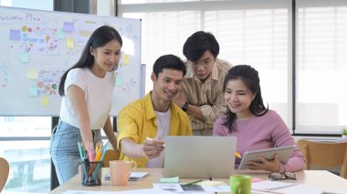 Genç girişimci takımı modern cihazlarla parlak ofiste birlikte çalışıyor..