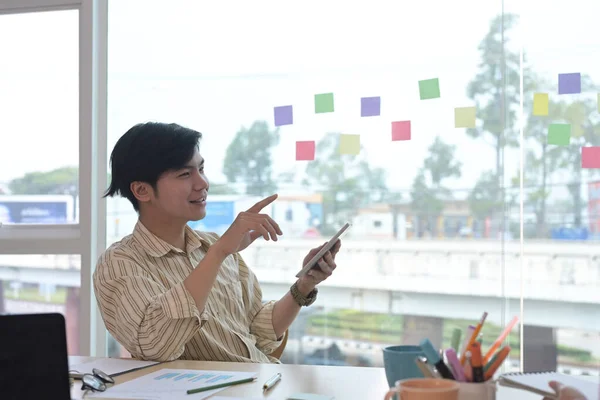 Knappe Aziatische zakenman zittend op creatieve werkplek en met behulp van digitale tablet. — Stockfoto