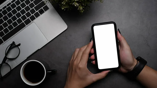 Mano de mujer sosteniendo teléfono inteligente con pantalla en blanco en el lugar de trabajo moderno. — Foto de Stock