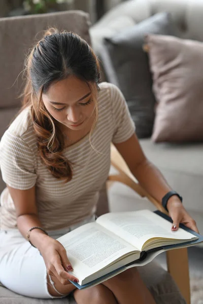 Enfocado hermosa mujer leyendo libro mientras está sentado en sillón en casa. — Foto de Stock