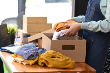 Kırpılmış küçük işletme sahibi müşterilere teslimat için karton kutuda ürün paketliyor. Online satış, e-ticaret