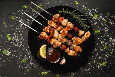 Tavuklu ızgara et şişleri ve siyah ahşap masa üzerinde barbekü sosu.