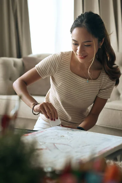 Hermosa artista femenina usando una espátula para difundir la pintura sobre su nueva pintura. — Foto de Stock