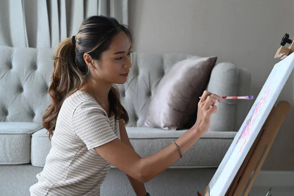 Relaxé jeune asiatique femme assis en face de chevalet et peinture tableau avec aquarelle. — Photo