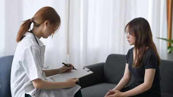 Vrouwelijke arts raadpleegt jonge patiënt en vulformulier in overleg. — Stockfoto