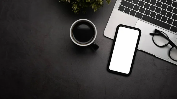 Мобильный телефон-макет с белым экраном, ноутбуком, чашкой для кофе и очками на черном столе. — стоковое фото
