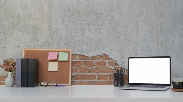 Laptop z pustym ekranem na białym stole na ścianie z cegły. — Zdjęcie stockowe