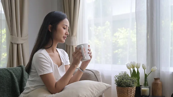 Tevreden jonge vrouw ontspannen op de bank en het drinken van hete koffie in de ochtend — Stockfoto