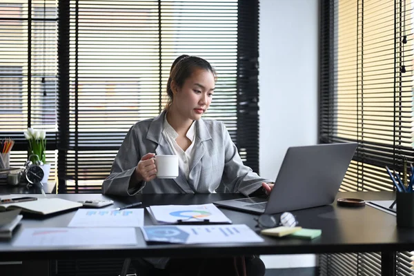 Agradable mujer de negocios que busca información en línea con el ordenador portátil en su estación de trabajo — Foto de Stock