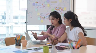 İki yaratıcı kadın dizüstü bilgisayara bakıyor, yeni projeyi tartışıyorlar.