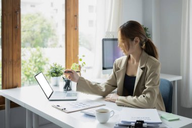 Düşünceli kadın finans müdürü parlak modern ofiste bilgisayar bilgisayarı üzerinde çalışıyor..