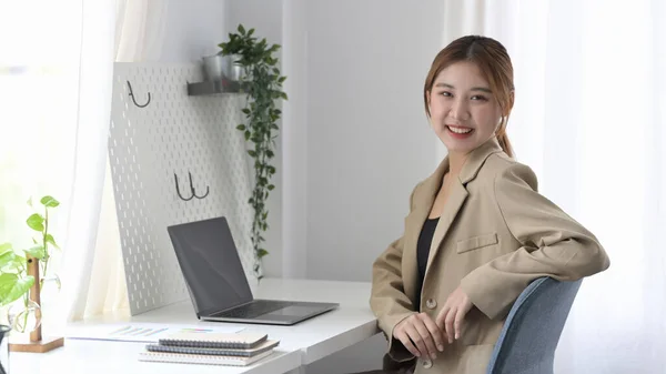 Freelancer feminino atraente sentado no escritório em casa e sorrindo para a câmera. — Fotografia de Stock