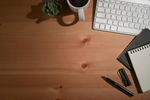 Eenvoudige werkplek met draadloos toetsenbord, notebook en koffiebeker op houten tafel. Bovenaanzicht. — Stockfoto