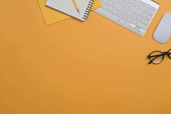 Ovanifrån trådlöst tangentbord, glasögon, mus och anteckningsbok på gul bakgrund med kopieringsutrymme för annonstext. — Stockfoto