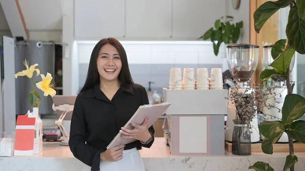 Proprietária bem sucedida do negócio do sexo feminino em pé atrás do balcão de café e sorrindo para a câmera. — Fotografia de Stock
