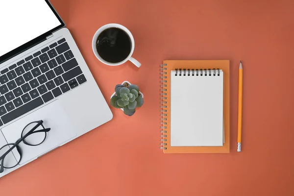 Top vista computador laptop, xícara de café, notebook e óculos no fundo laranja. — Fotografia de Stock