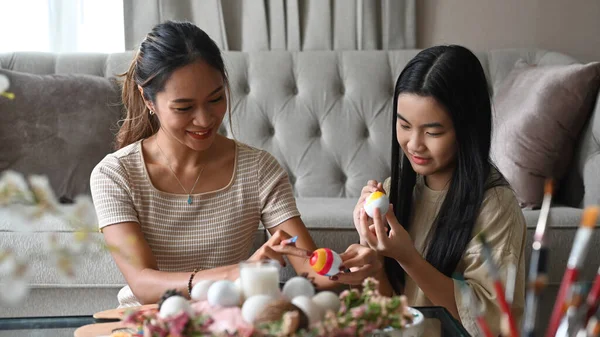 Piękna azjatycka matka i jej córka świętują Wielkanoc, malując razem jajka. Pojęcie świąt wielkanocnych. — Zdjęcie stockowe