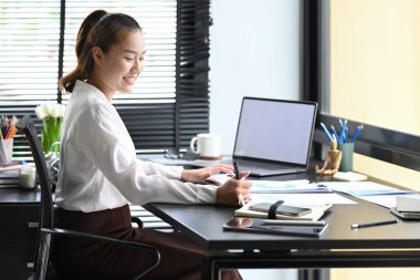 Dizüstü bilgisayar kullanan ve not defterine önemli bilgiler yazan kadın muhasebeci..