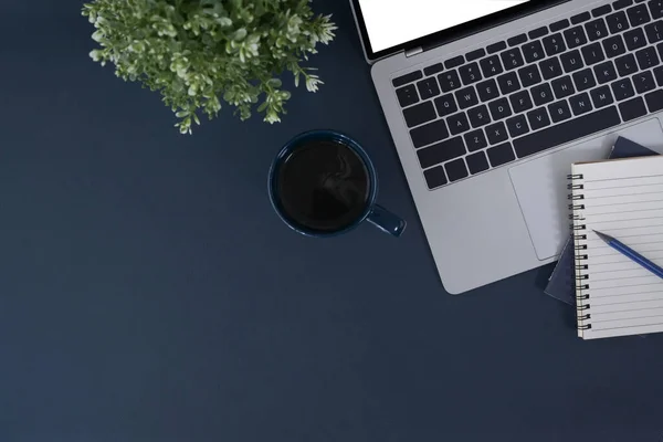 Stylish workspace with laptop computer, notebook and coffee cup on dark blue background. Top view, flat lay.