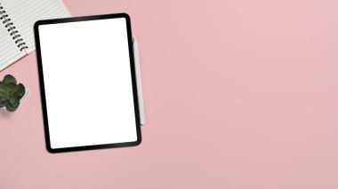 Dijital tableti, defteri ve pembe arka planda sulu bitkisi olan kadınsı bir iş yeri. Kopyalama alanı olan üst görünüm.