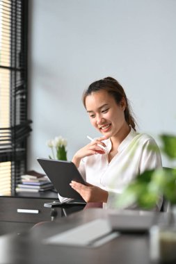 Parlak modern iş yerinde dijital tablet kullanan düşünceli bir bayan yönetici..