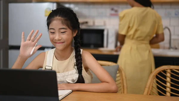 Smiling Asian girl having online class on computer tablet at home. Concept of Virtual education, homeschooling.