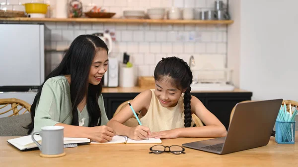 Asian mom helping her daughter doing homework. Concept of Virtual education, homeschooling.