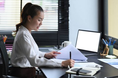 Asyalı bayan yönetici dizüstü bilgisayarda oturuyor ve mali raporları kontrol ediyor..