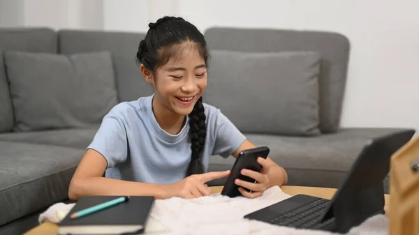 Cheerful Asian girl using smart phone during break from learning online. E-learning, homeschooling concept.