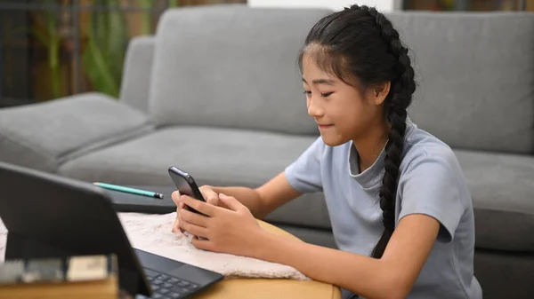 Asian girl searching information on smart phone during learning online in virtual classroom. E-learning, homeschooling concept.