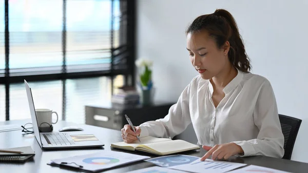 Focused Asian Businesswoman Analyzing Financial Graph Making Notes Notebook — Stock Photo, Image